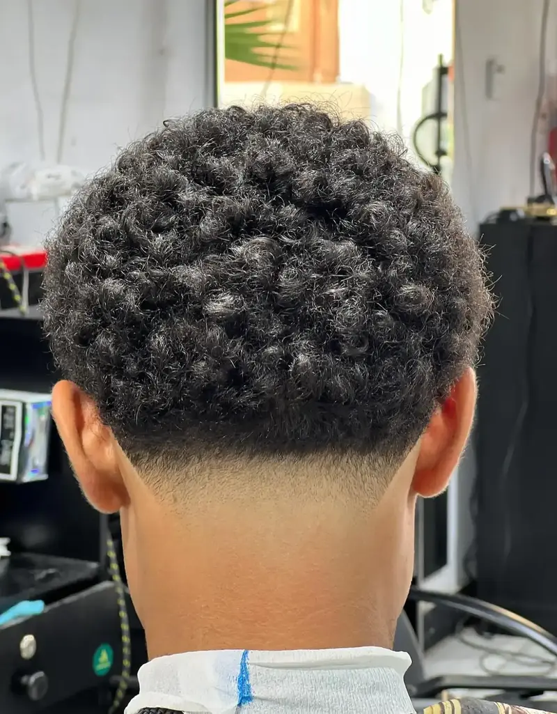 Close-up of a low taper fade haircut with tight curls, showcasing the back view in a barbershop setting.