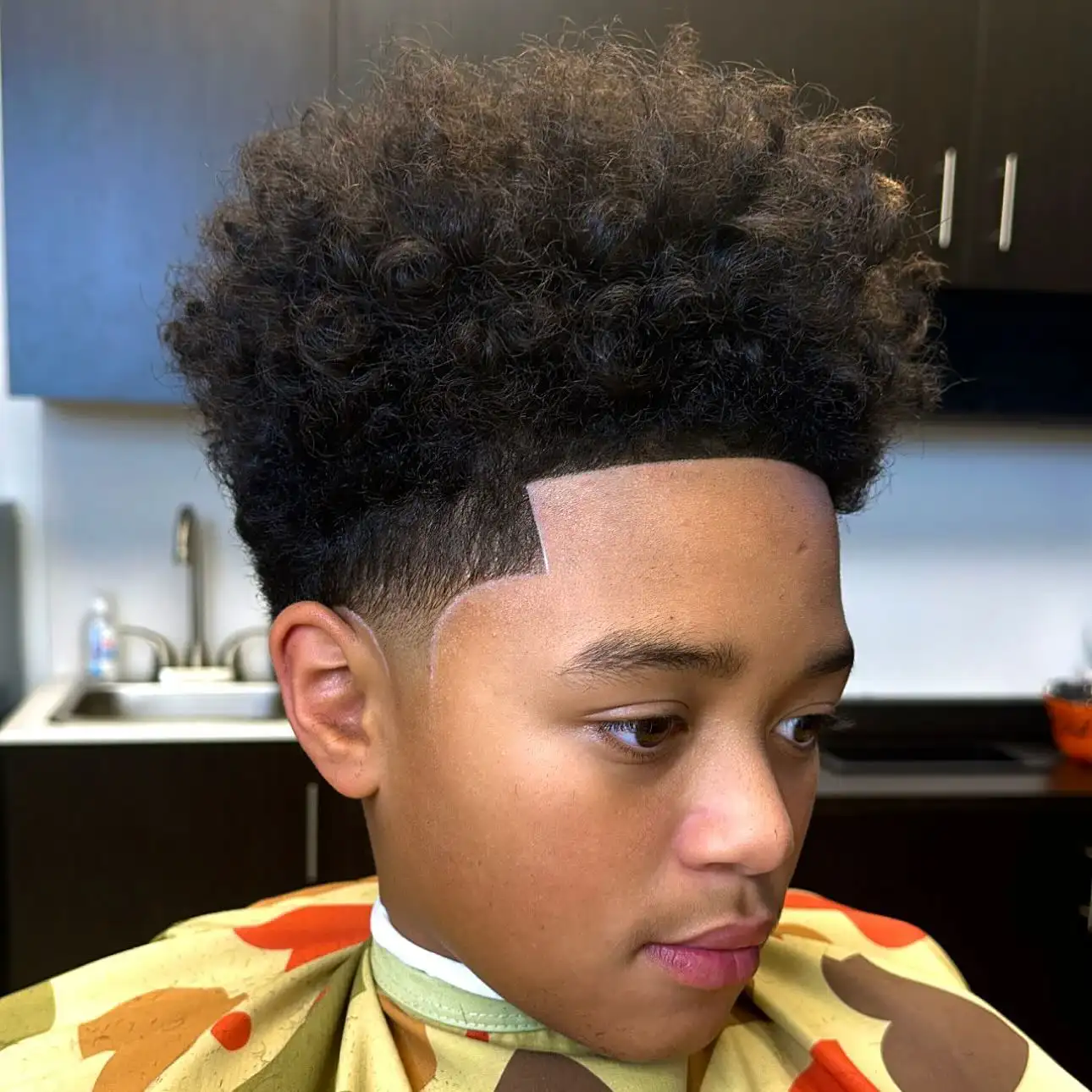 A person with a fresh haircut featuring a curly high top and a low taper, sitting in a barbershop chair.