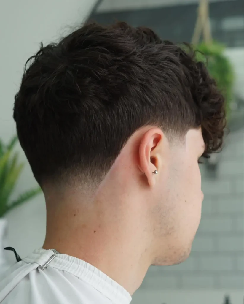 A person with a low taper fade haircut and loose curls, viewed from the back, showcasing a stylish and modern hairstyle.