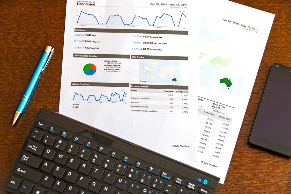 Free Flatlay of a business analytics report, keyboard, pen, and smartphone on a wooden desk. Stock Photo